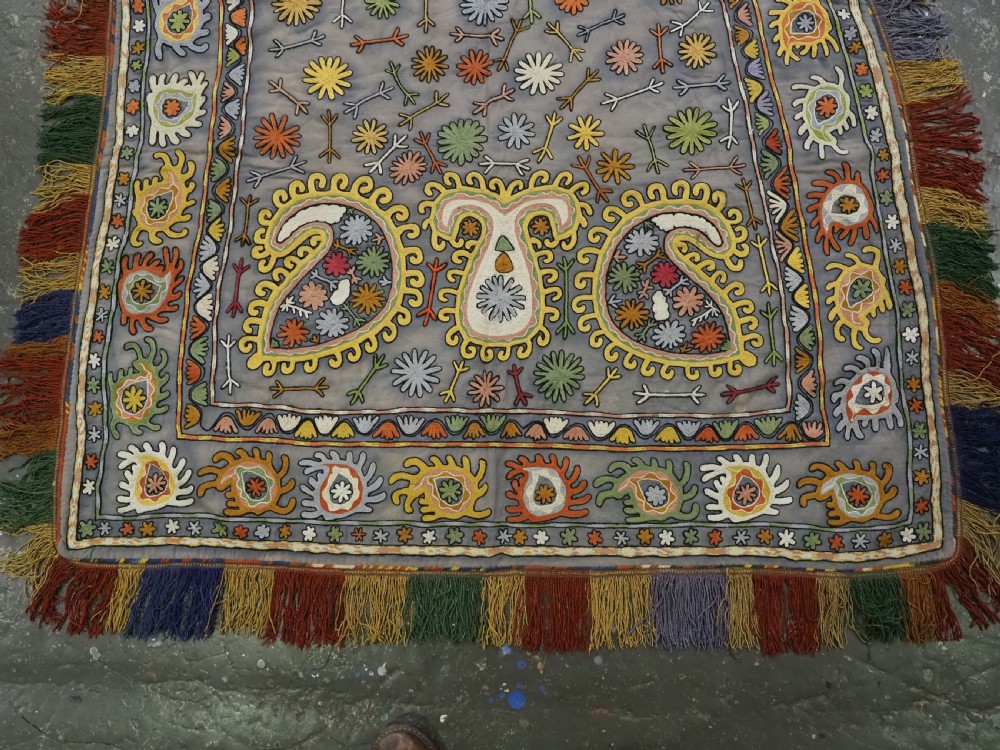 An early 20th-century Uzbek Lakai embroidered saddle cover featuring vibrant silk boteh and floral motifs on a grey ground with colourful fringe trim. View IV