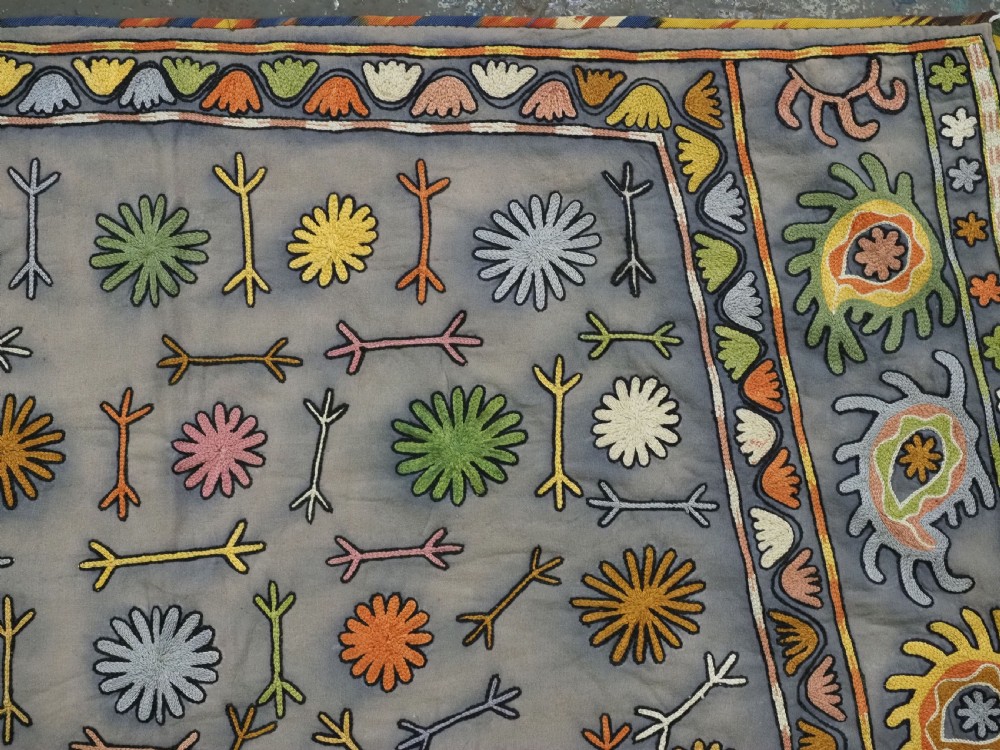 An early 20th-century Uzbek Lakai embroidered saddle cover featuring vibrant silk boteh and floral motifs on a grey ground with colourful fringe trim. View VI