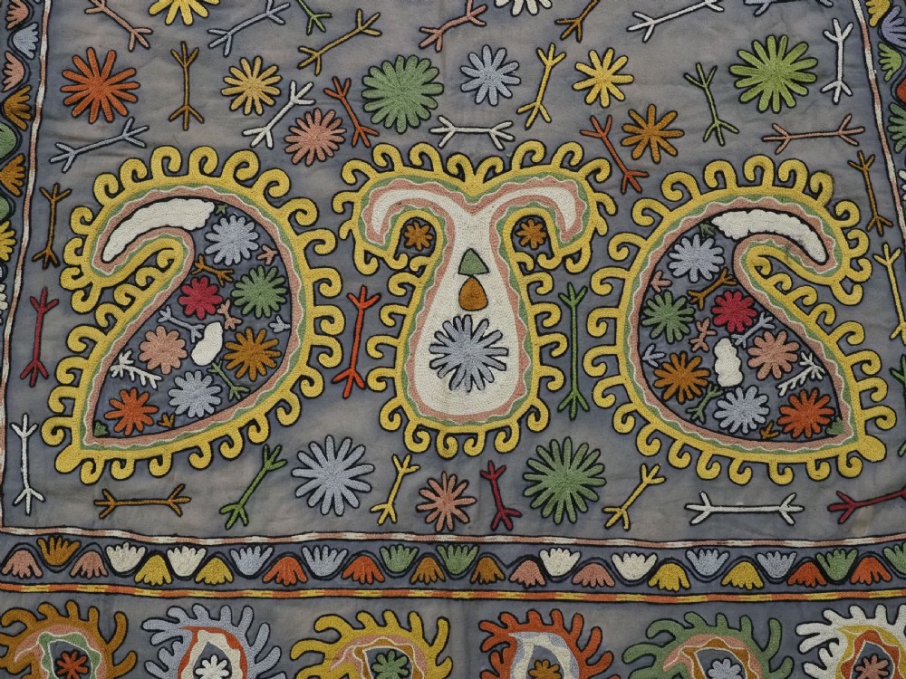 An early 20th-century Uzbek Lakai embroidered saddle cover featuring vibrant silk boteh and floral motifs on a grey ground with colourful fringe trim. View VIII