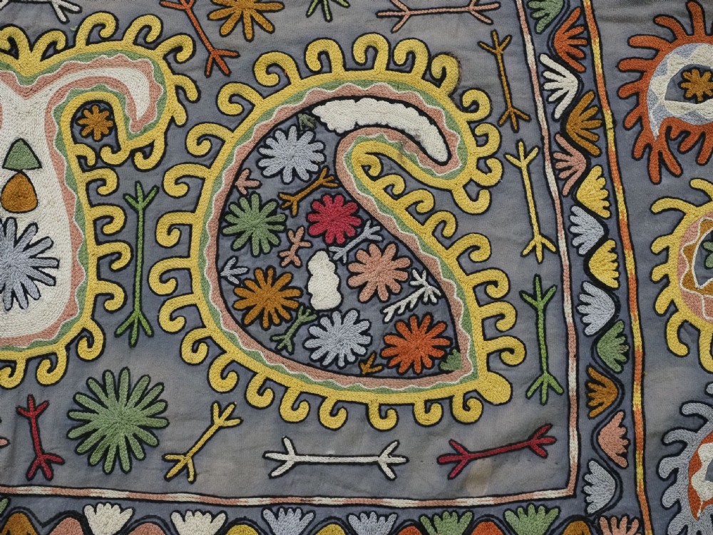 An early 20th-century Uzbek Lakai embroidered saddle cover featuring vibrant silk boteh and floral motifs on a grey ground with colourful fringe trim. View XI
