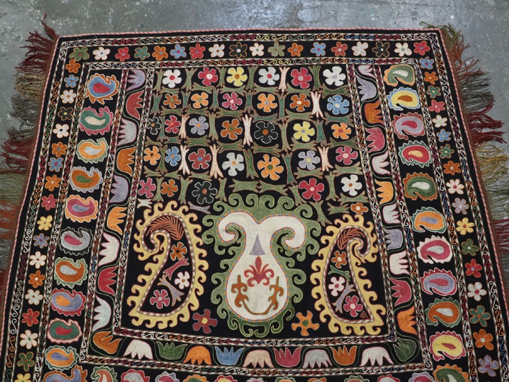 A square black textile decorated with dense multicoloured silk embroidery displaying floral and paisley motifs with fringed edges. View III