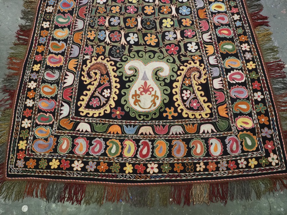A square black textile decorated with dense multicoloured silk embroidery displaying floral and paisley motifs with fringed edges. View IV