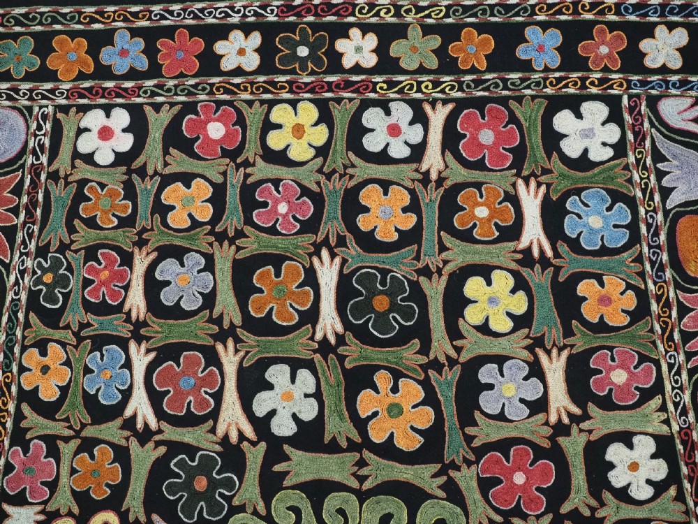 A square black textile decorated with dense multicoloured silk embroidery displaying floral and paisley motifs with fringed edges. View VI