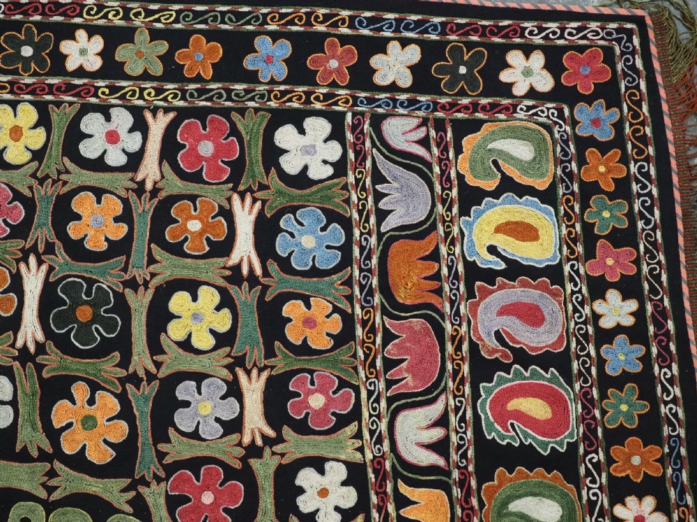 A square black textile decorated with dense multicoloured silk embroidery displaying floral and paisley motifs with fringed edges. View VII