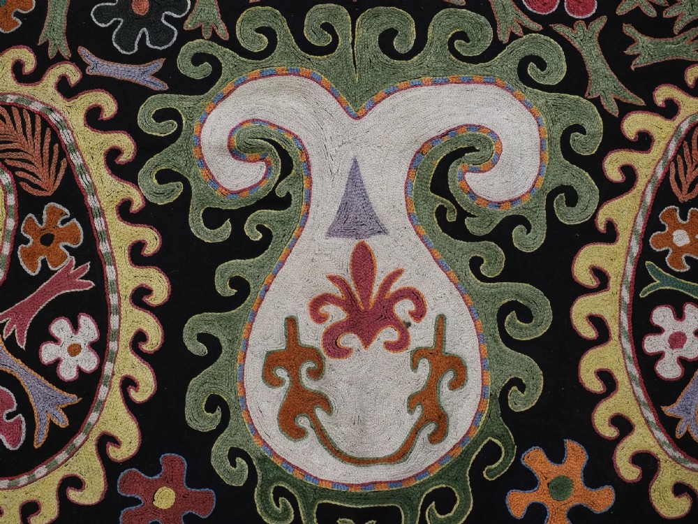 A square black textile decorated with dense multicoloured silk embroidery displaying floral and paisley motifs with fringed edges. View IX