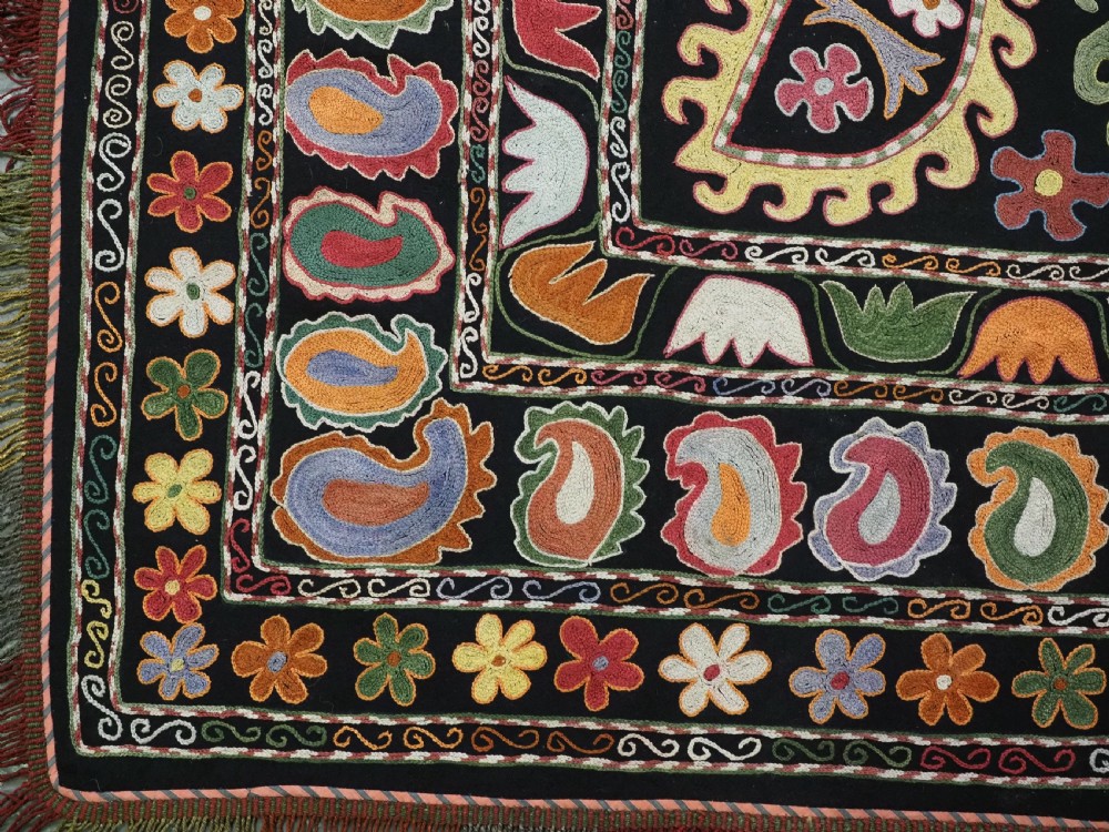 A square black textile decorated with dense multicoloured silk embroidery displaying floral and paisley motifs with fringed edges. View XI