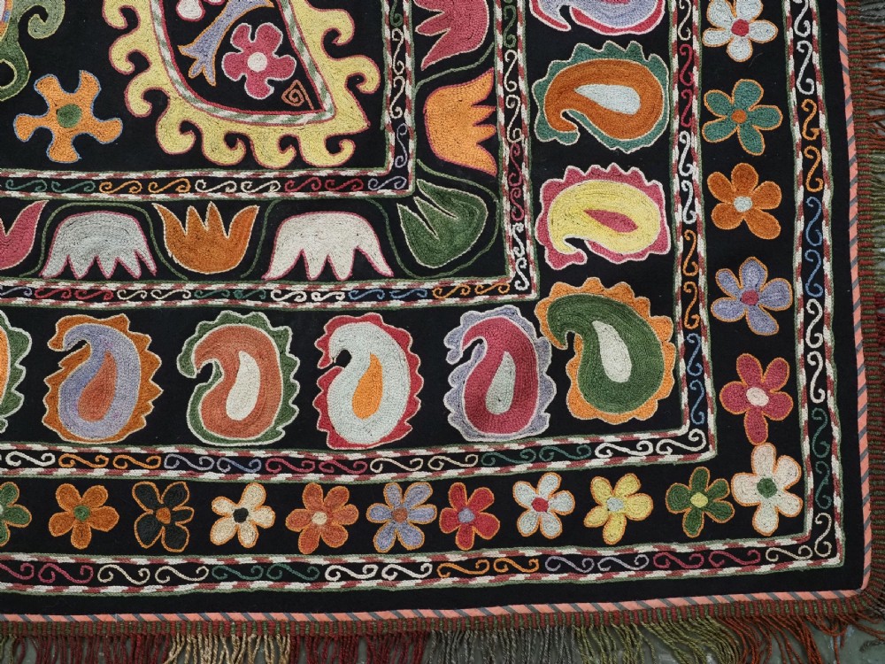 A square black textile decorated with dense multicoloured silk embroidery displaying floral and paisley motifs with fringed edges. View XIII