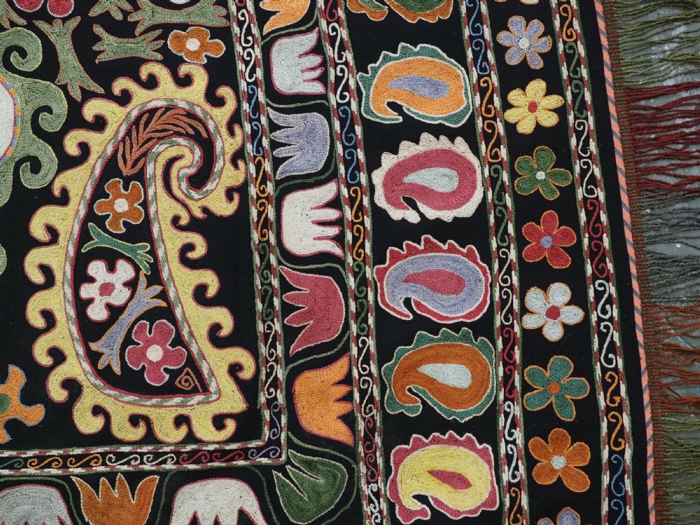 A square black textile decorated with dense multicoloured silk embroidery displaying floral and paisley motifs with fringed edges. View XIV