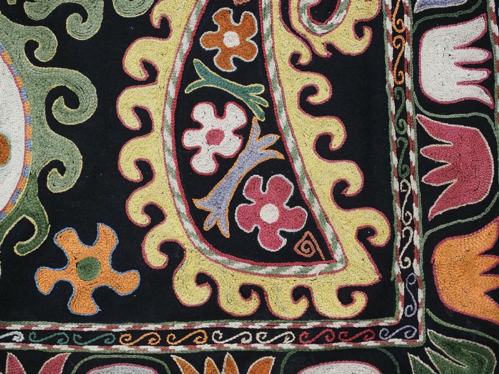 A square black textile decorated with dense multicoloured silk embroidery displaying floral and paisley motifs with fringed edges. View XV