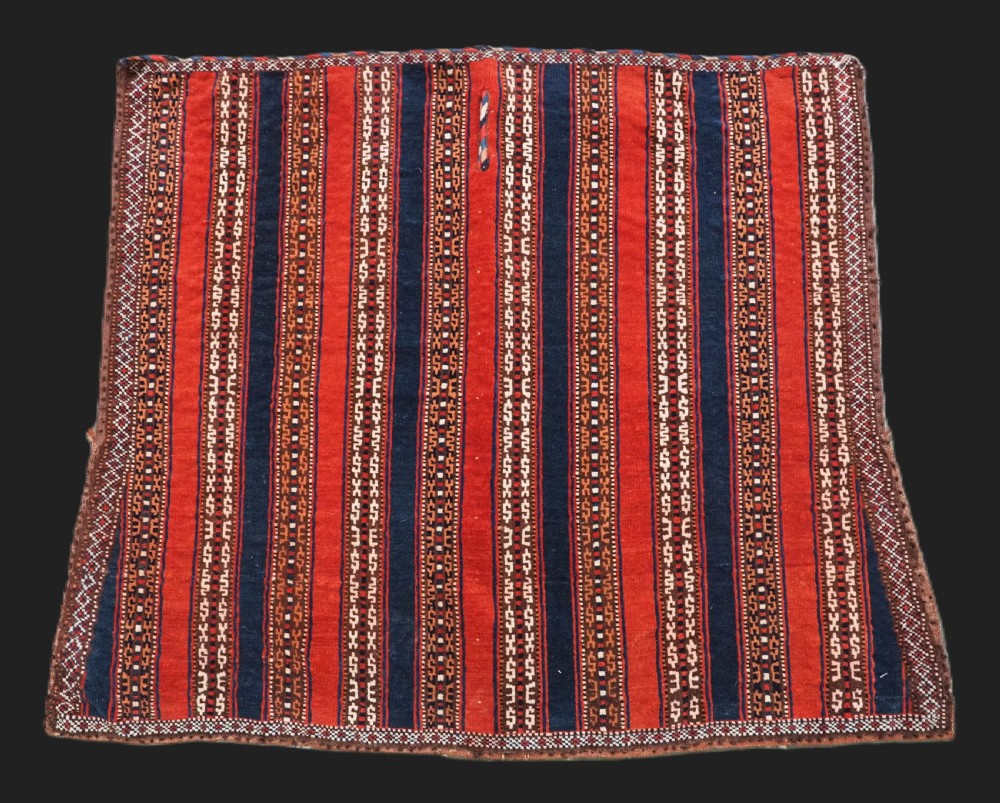 An antique square Turkmen Yomut saddle rug featuring vertical red and navy blue stripes with geometric tribal patterns and woven borders.