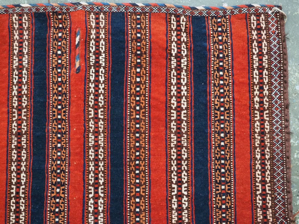 An antique square Turkmen Yomut saddle rug featuring vertical red and navy blue stripes with geometric tribal patterns and woven borders. View III