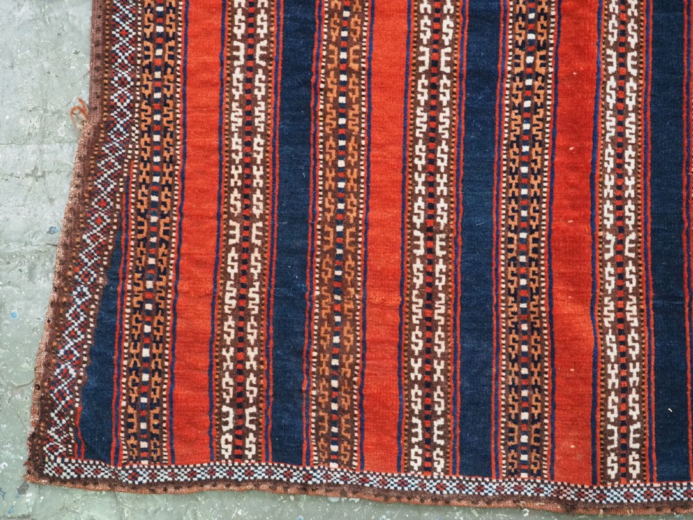 An antique square Turkmen Yomut saddle rug featuring vertical red and navy blue stripes with geometric tribal patterns and woven borders. View IV
