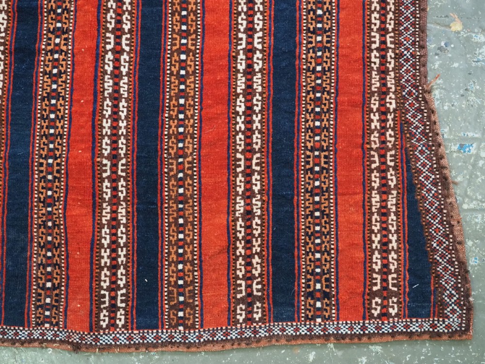 An antique square Turkmen Yomut saddle rug featuring vertical red and navy blue stripes with geometric tribal patterns and woven borders. View V
