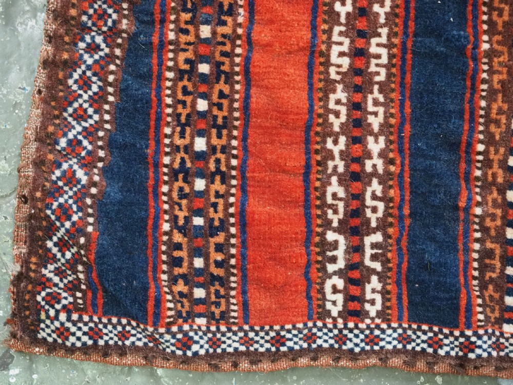 An antique square Turkmen Yomut saddle rug featuring vertical red and navy blue stripes with geometric tribal patterns and woven borders. View VII