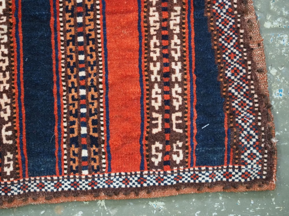 An antique square Turkmen Yomut saddle rug featuring vertical red and navy blue stripes with geometric tribal patterns and woven borders. View VIII