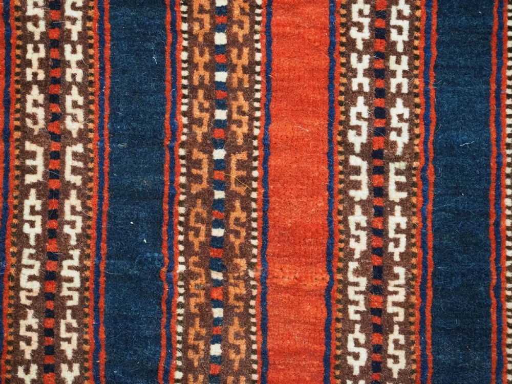 An antique square Turkmen Yomut saddle rug featuring vertical red and navy blue stripes with geometric tribal patterns and woven borders. View IX