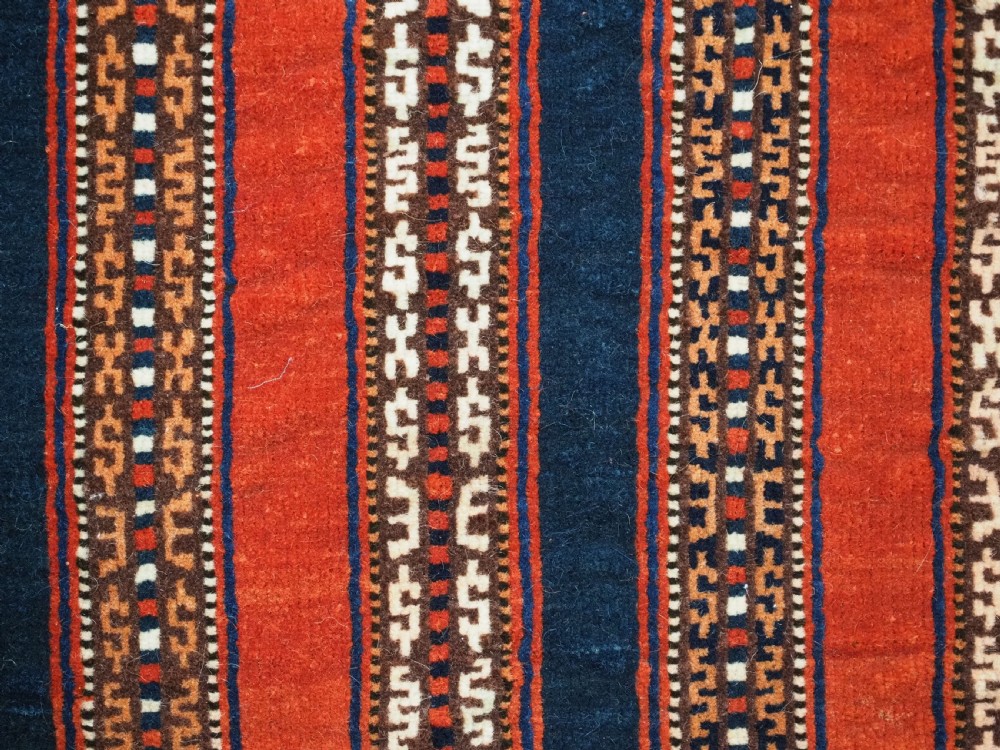 An antique square Turkmen Yomut saddle rug featuring vertical red and navy blue stripes with geometric tribal patterns and woven borders. View X