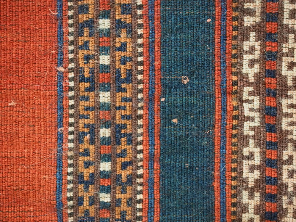 An antique square Turkmen Yomut saddle rug featuring vertical red and navy blue stripes with geometric tribal patterns and woven borders. View XII