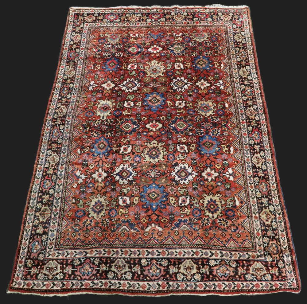 An antique Persian Mahal hand-knotted wool carpet featuring a red central field decorated with an all-over palmette motif and multi-tiered patterned borders.