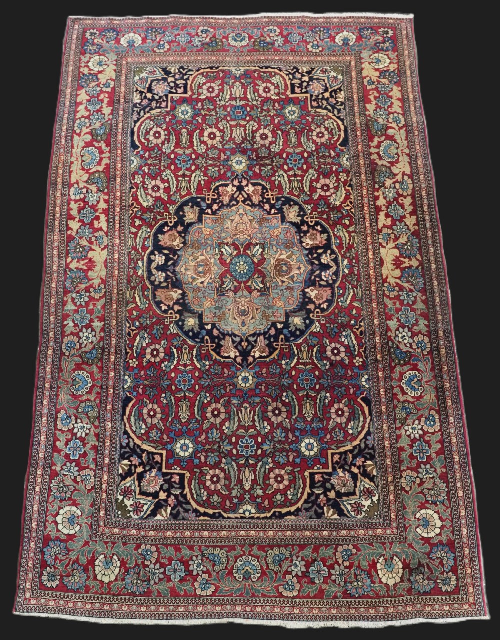 An antique hand-knotted Persian Isfahan wool carpet featuring a central starburst medallion surrounded by dense floral vine motifs in red, navy blue, and cream.