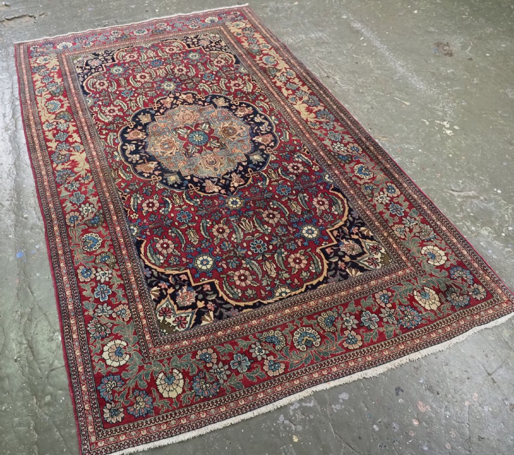 An antique hand-knotted Persian Isfahan wool carpet featuring a central starburst medallion surrounded by dense floral vine motifs in red, navy blue, and cream. View II