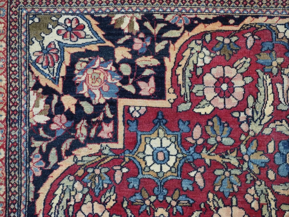 An antique hand-knotted Persian Isfahan wool carpet featuring a central starburst medallion surrounded by dense floral vine motifs in red, navy blue, and cream. View VIII