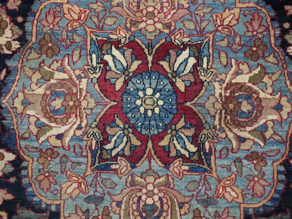 An antique hand-knotted Persian Isfahan wool carpet featuring a central starburst medallion surrounded by dense floral vine motifs in red, navy blue, and cream. View XII