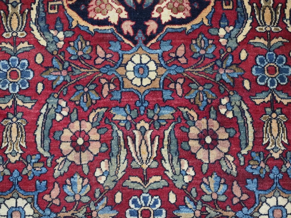 An antique hand-knotted Persian Isfahan wool carpet featuring a central starburst medallion surrounded by dense floral vine motifs in red, navy blue, and cream. View XIII