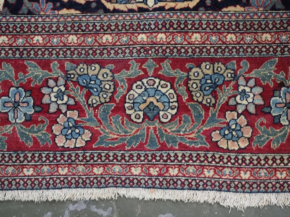 An antique hand-knotted Persian Isfahan wool carpet featuring a central starburst medallion surrounded by dense floral vine motifs in red, navy blue, and cream. View XIV