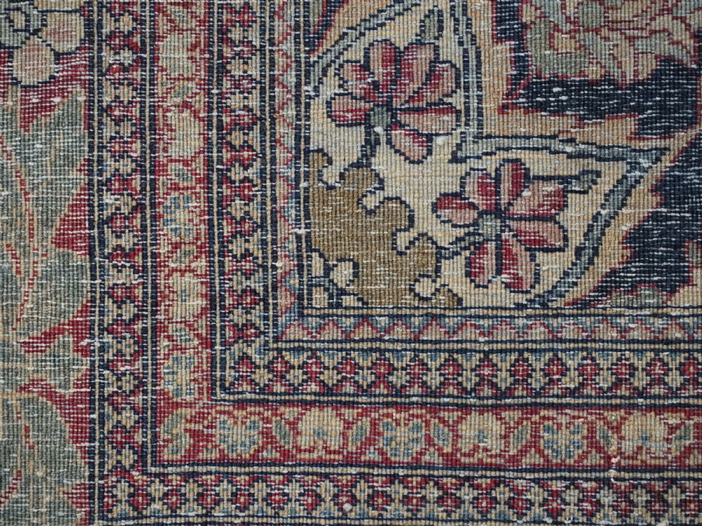An antique hand-knotted Persian Isfahan wool carpet featuring a central starburst medallion surrounded by dense floral vine motifs in red, navy blue, and cream. View XVI