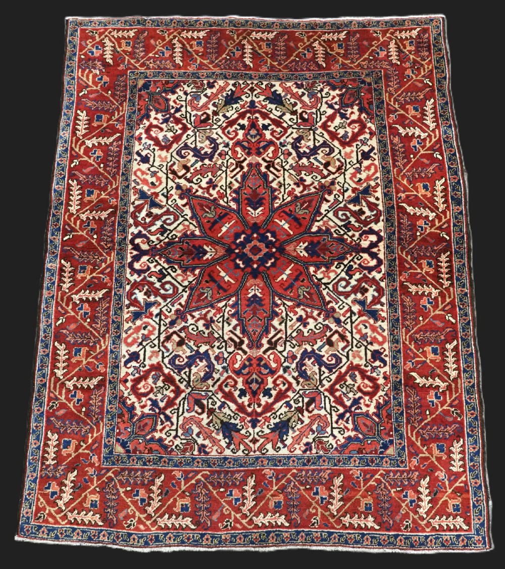 An antique hand-knotted Persian Heriz wool rug featuring a central eight-pointed red star medallion on an ivory ground with a detailed geometric red border.