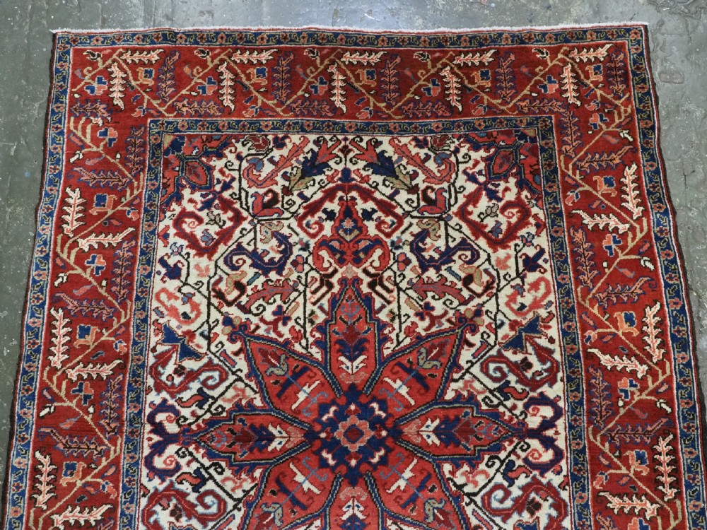An antique hand-knotted Persian Heriz wool rug featuring a central eight-pointed red star medallion on an ivory ground with a detailed geometric red border. View III