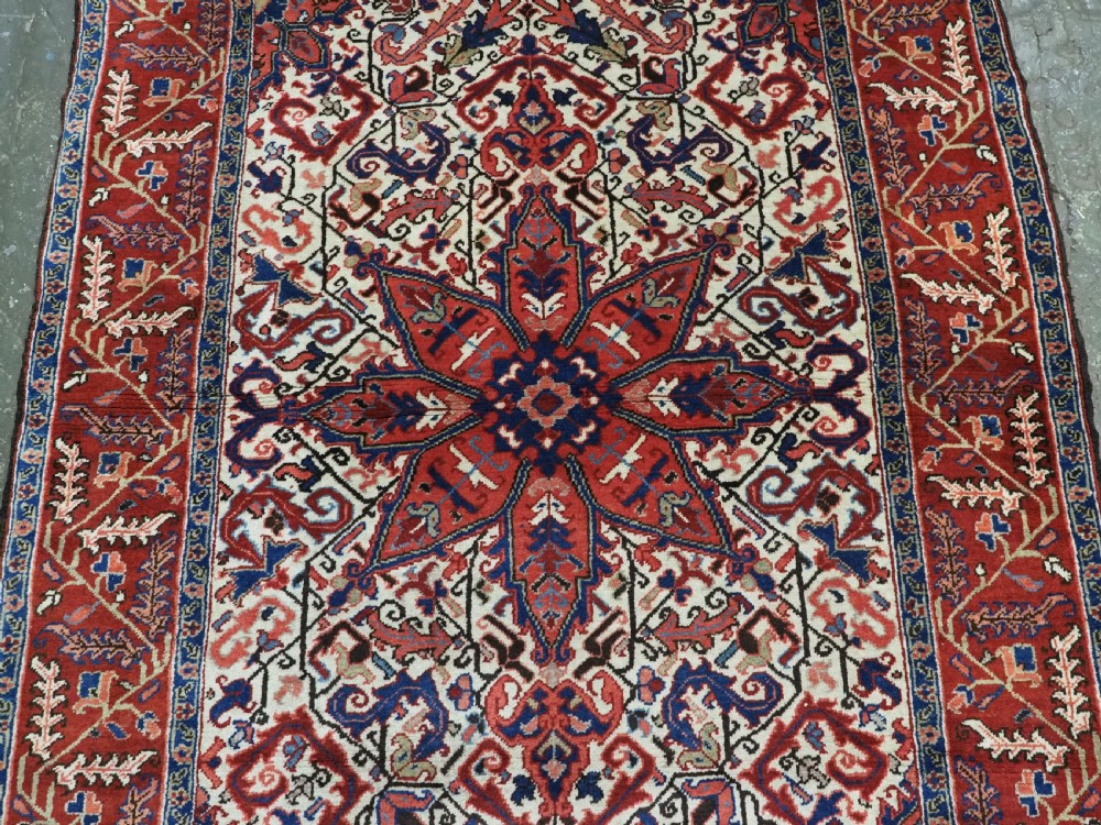 An antique hand-knotted Persian Heriz wool rug featuring a central eight-pointed red star medallion on an ivory ground with a detailed geometric red border. View IV