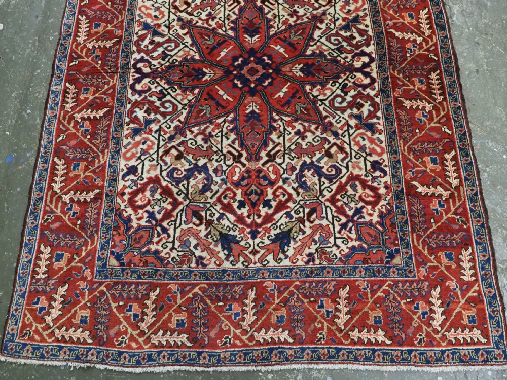 An antique hand-knotted Persian Heriz wool rug featuring a central eight-pointed red star medallion on an ivory ground with a detailed geometric red border. View V