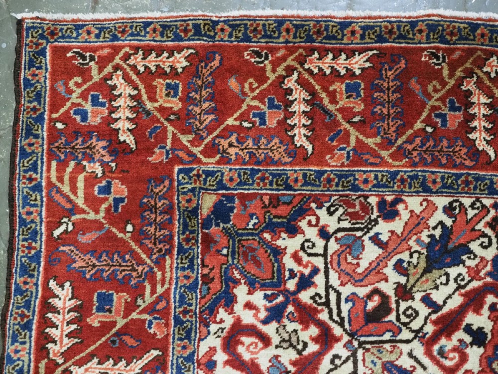An antique hand-knotted Persian Heriz wool rug featuring a central eight-pointed red star medallion on an ivory ground with a detailed geometric red border. View VI