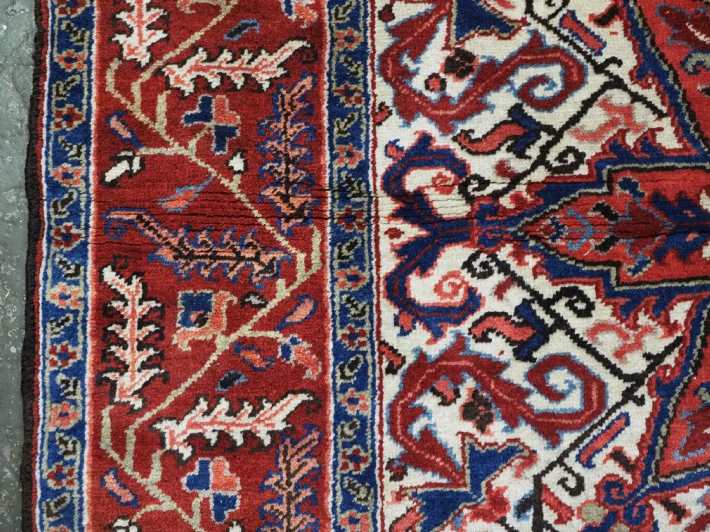 An antique hand-knotted Persian Heriz wool rug featuring a central eight-pointed red star medallion on an ivory ground with a detailed geometric red border. View VII
