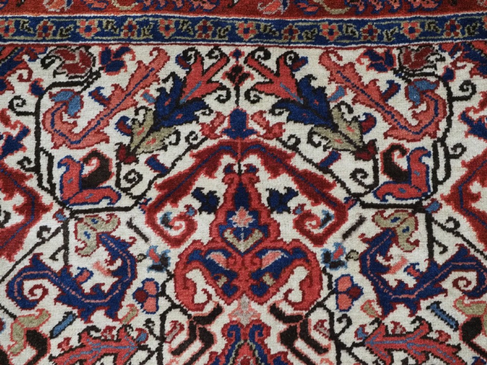 An antique hand-knotted Persian Heriz wool rug featuring a central eight-pointed red star medallion on an ivory ground with a detailed geometric red border. View VIII