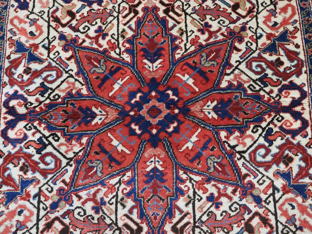 An antique hand-knotted Persian Heriz wool rug featuring a central eight-pointed red star medallion on an ivory ground with a detailed geometric red border. View IX