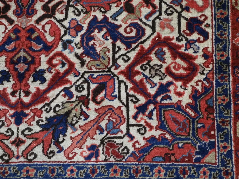 An antique hand-knotted Persian Heriz wool rug featuring a central eight-pointed red star medallion on an ivory ground with a detailed geometric red border. View XII