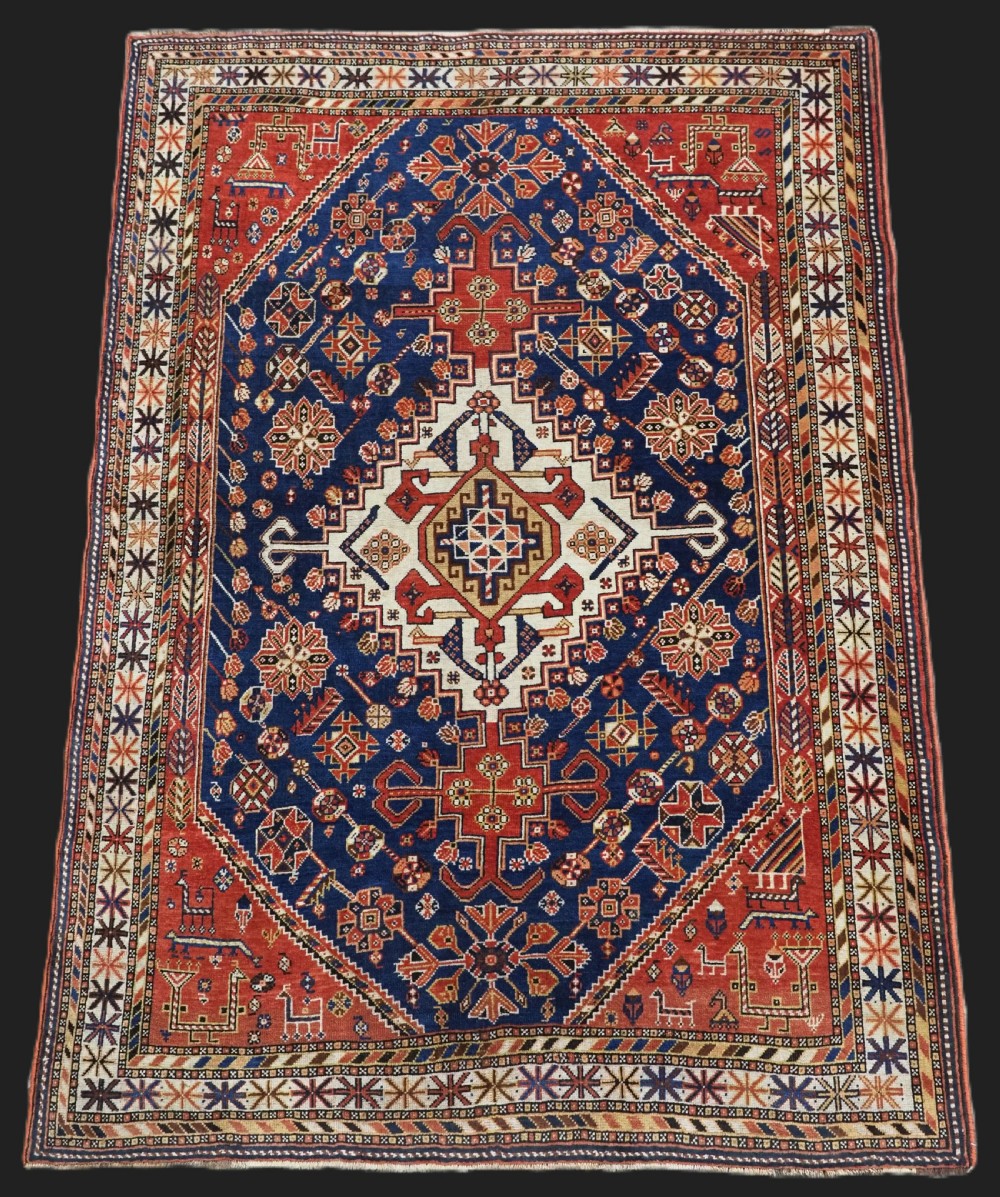 An antique hand-knotted Qashqai tribal rug featuring a central stepped diamond medallion in navy blue, red, and ivory surrounded by geometric peacock figures.