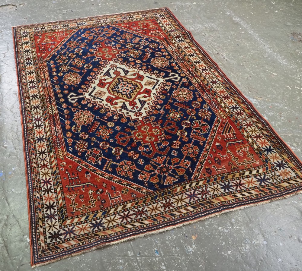 An antique hand-knotted Qashqai tribal rug featuring a central stepped diamond medallion in navy blue, red, and ivory surrounded by geometric peacock figures. View II