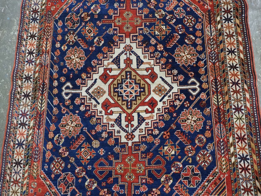 An antique hand-knotted Qashqai tribal rug featuring a central stepped diamond medallion in navy blue, red, and ivory surrounded by geometric peacock figures. View IV
