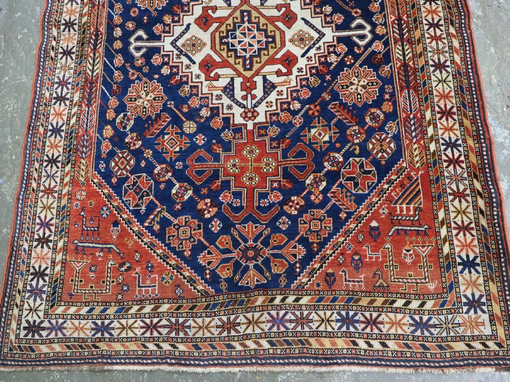 An antique hand-knotted Qashqai tribal rug featuring a central stepped diamond medallion in navy blue, red, and ivory surrounded by geometric peacock figures. View V