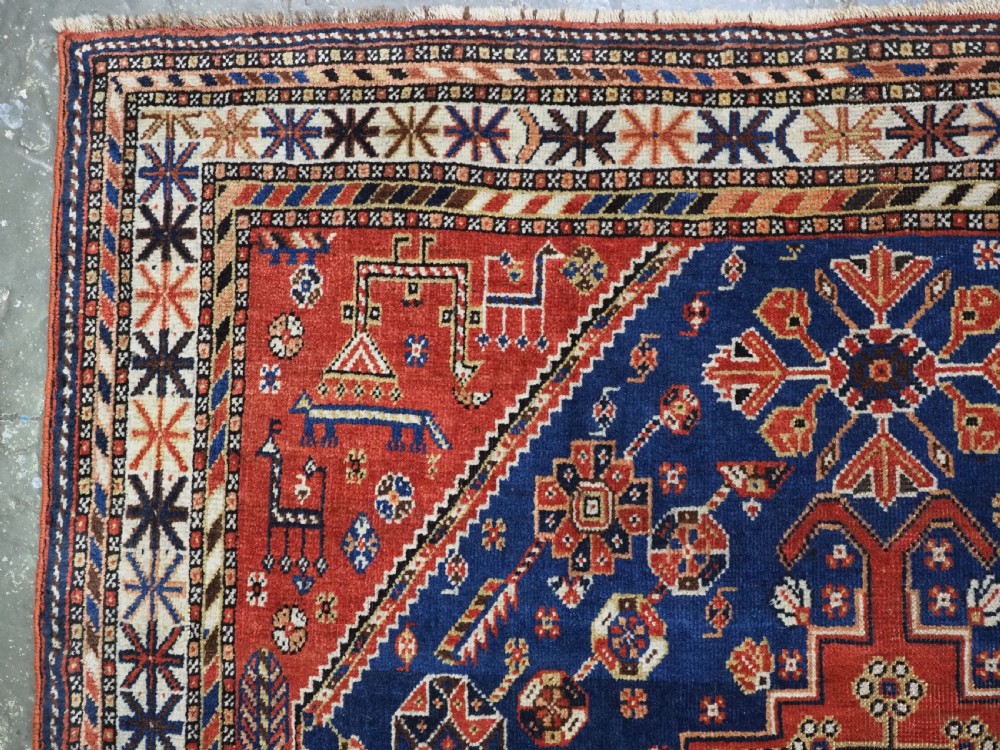 An antique hand-knotted Qashqai tribal rug featuring a central stepped diamond medallion in navy blue, red, and ivory surrounded by geometric peacock figures. View VI