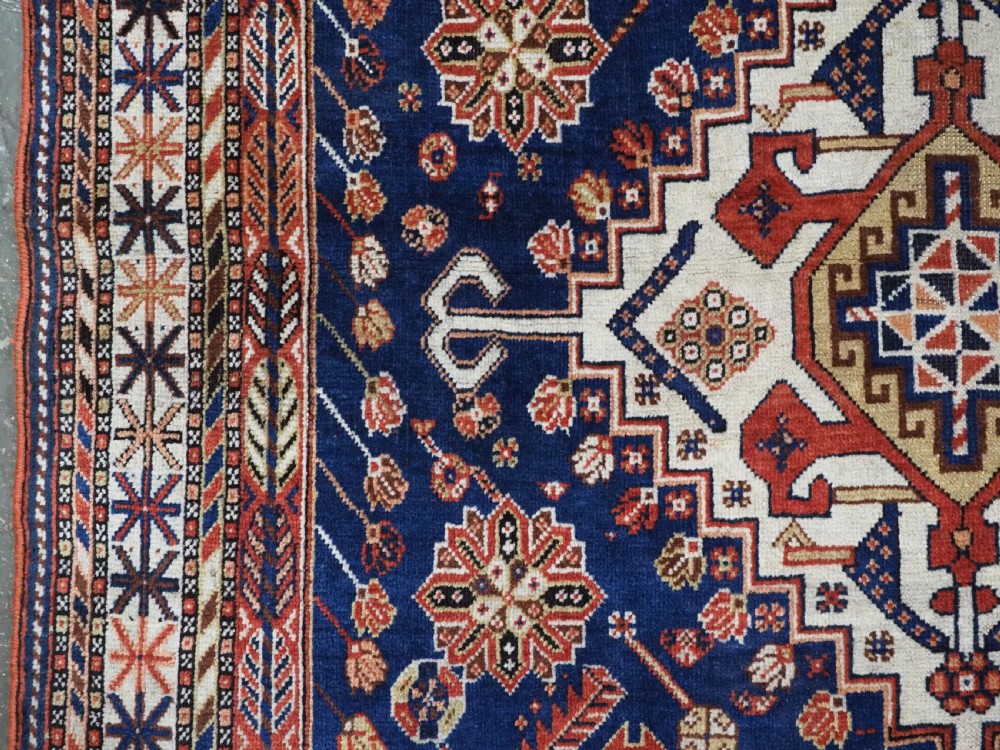 An antique hand-knotted Qashqai tribal rug featuring a central stepped diamond medallion in navy blue, red, and ivory surrounded by geometric peacock figures. View VII