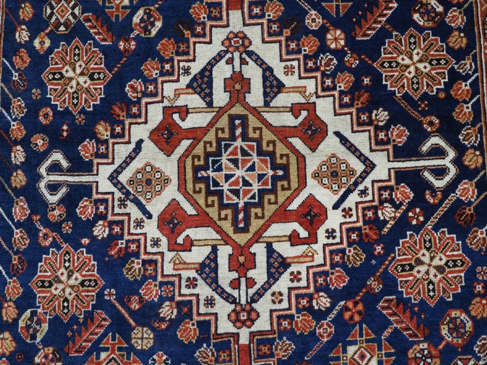An antique hand-knotted Qashqai tribal rug featuring a central stepped diamond medallion in navy blue, red, and ivory surrounded by geometric peacock figures. View IX