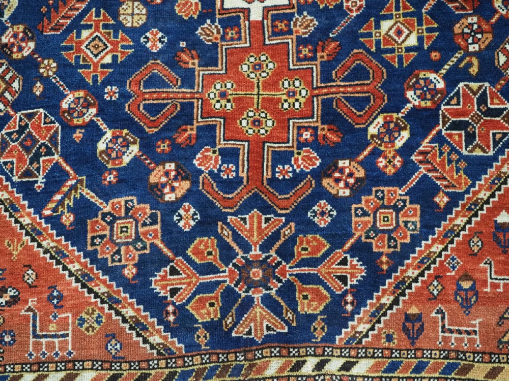 An antique hand-knotted Qashqai tribal rug featuring a central stepped diamond medallion in navy blue, red, and ivory surrounded by geometric peacock figures. View X