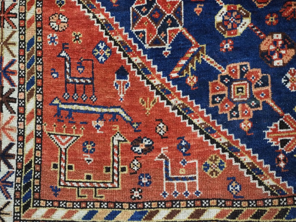 An antique hand-knotted Qashqai tribal rug featuring a central stepped diamond medallion in navy blue, red, and ivory surrounded by geometric peacock figures. View XII