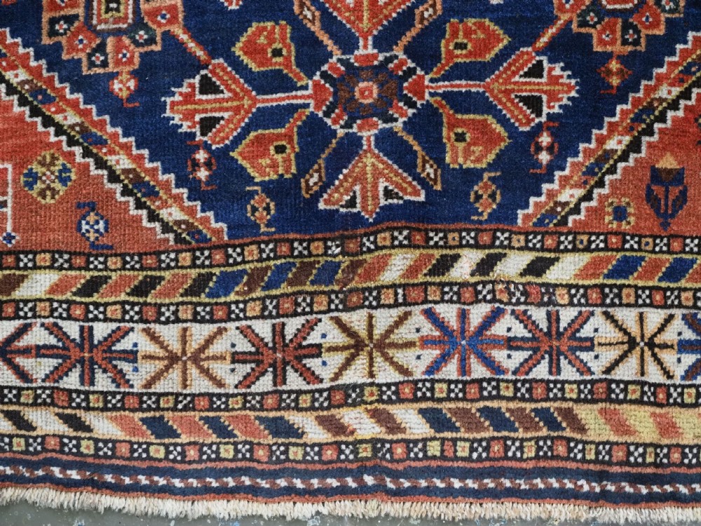 An antique hand-knotted Qashqai tribal rug featuring a central stepped diamond medallion in navy blue, red, and ivory surrounded by geometric peacock figures. View XIII