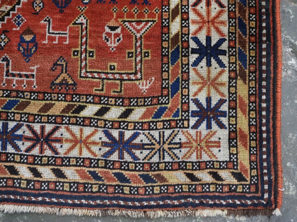 An antique hand-knotted Qashqai tribal rug featuring a central stepped diamond medallion in navy blue, red, and ivory surrounded by geometric peacock figures. View XIV